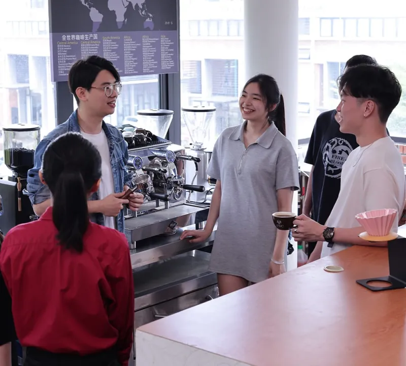 Students receiving hands-on guidance beside an espresso machine
